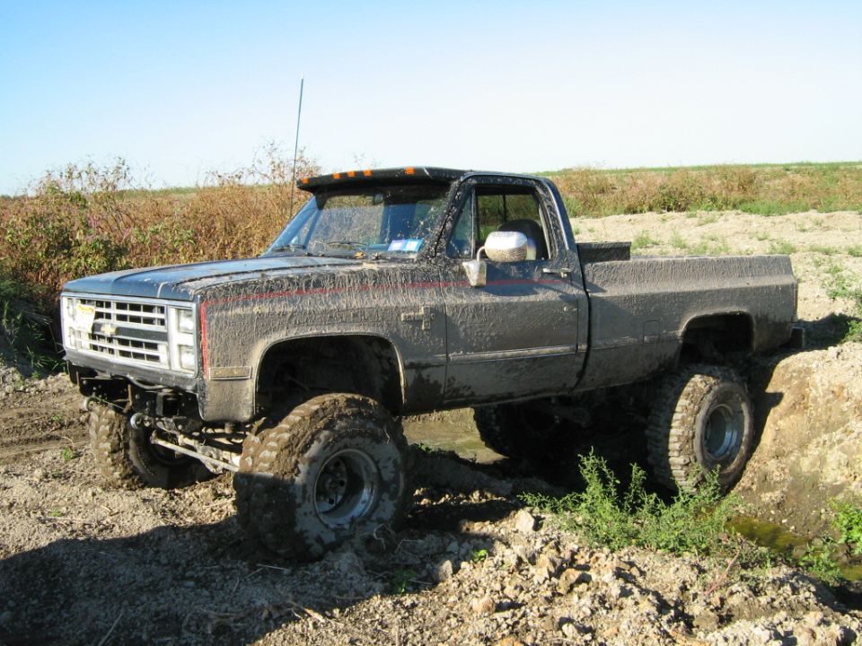 Mud-covered pickup truck with lifted suspension and large tires driving off-road