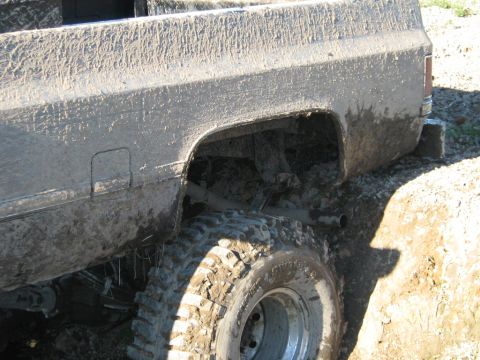 1990 Ford Bronco - This pickup truck is heavily covered in mud, showing its rear wheel and suspension system.