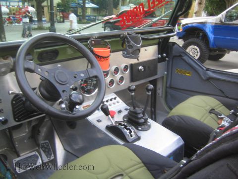 1990 Ford Bronco - stripped interior of a custom off-roader showing aluminum dash, gauge cluster, twin shift levers and green-trimmed seats.