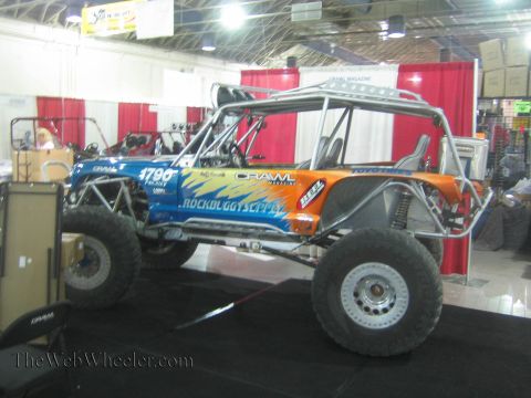 1990 Ford Bronco - blue and orange tube-chassis rock buggy number 17.90 on Toyo tires displayed at an indoor expo booth.