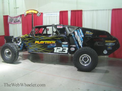 1990 Ford Bronco - black Playtech Racing tube-chassis off-road buggy number 123 with yellow flames and blue shocks on display indoors.