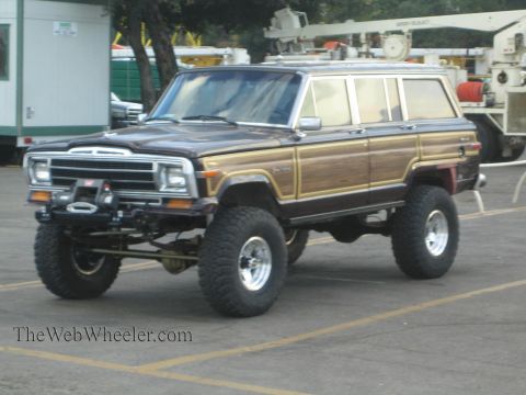 1990 Ford Bronco - brown lifted Jeep Grand Wagoneer with woodgrain side panels, front winch and chrome wheels parked outdoors.