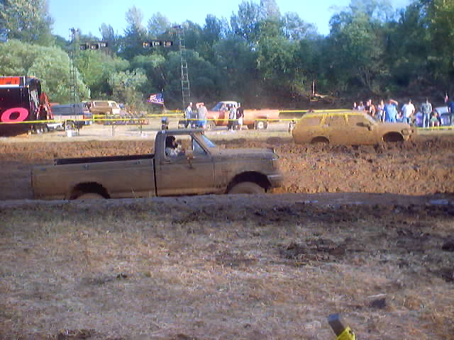 Truck stuck in mud, another SUV stuck in mud behind it, people watching