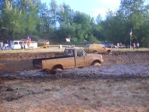 1976 Ford F-100 - Multiple vehicles are stuck in the mud during a competition, with spectators watching from the sidelines.
