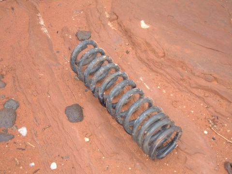 1993 Ford Bronco - A single coil spring rests on the red dirt terrain.