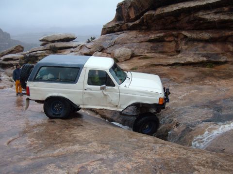 1993 Ford Bronco - A white Ford Bronco navigates a rocky, wet terrain with a person standing nearby.