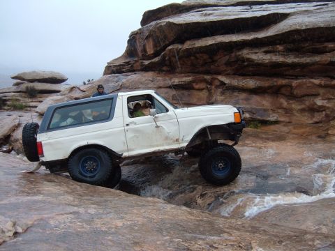 1993 Ford Bronco - White 1993 Ford Bronco navigating a challenging off-road course with water and large rocks.