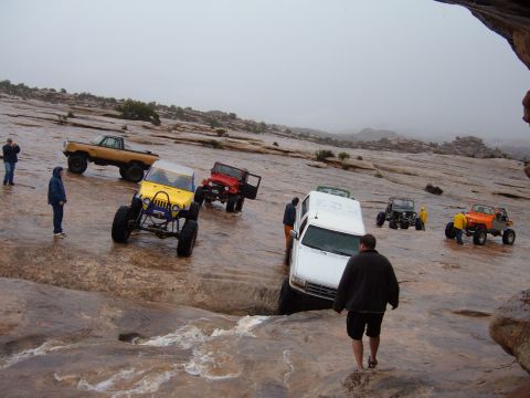 1993 Ford Bronco - Several off-road vehicles, including a 1993 Ford Bronco, traverse a wet, rocky terrain.