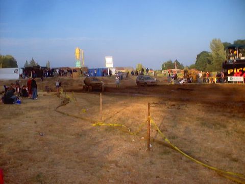 1976 Ford F-100 - Spectators watch vehicles navigate a muddy course during an outdoor event.