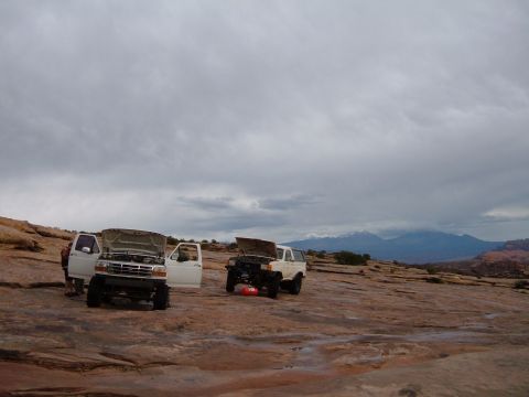1993 Ford Bronco - Several off-road vehicles are stopped on a rocky landscape under a cloudy sky, with mountains visible in the distance.