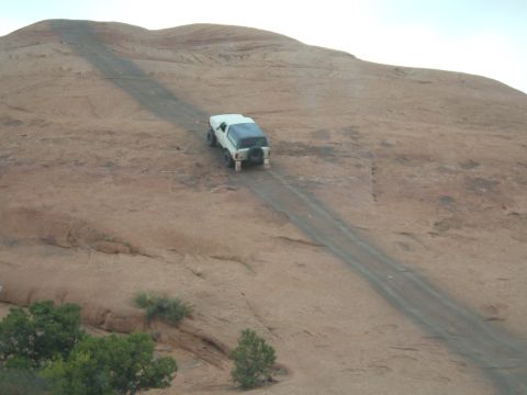 1993 Ford Bronco - A white 1993 Ford Bronco navigates a steep dirt track in a desert landscape.