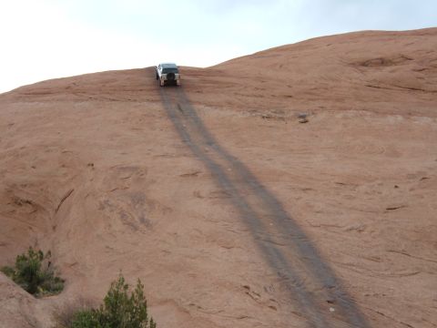 1993 Ford Bronco - A vehicle navigates a steep, dusty trail on a desert landscape under a bright sky.