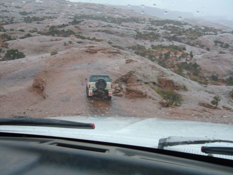 1993 Ford Bronco - A white SUV navigates a wet, rocky trail in a desolate landscape.