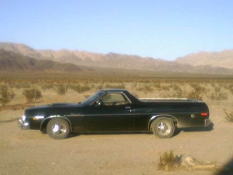 1973 Ford Ranchero - A black 1973 Ford Ranchero is parked on a dirt road with mountains in the background.