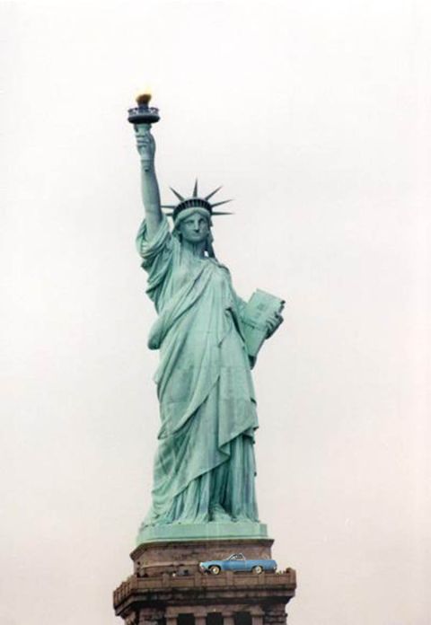 1971 Ford Ranchero - The Statue of Liberty stands tall with a small blue car placed on its pedestal, and a website logo at the bottom.