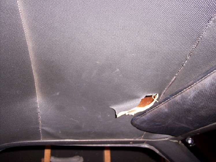 Torn hole in a black car headliner near the rear side trim panel