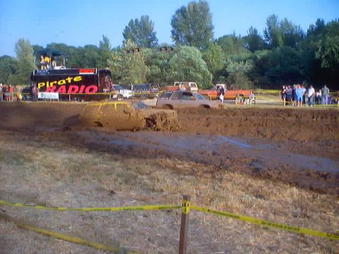 1976 Ford F-100 - Vehicles navigate a muddy obstacle course during a mud run event.