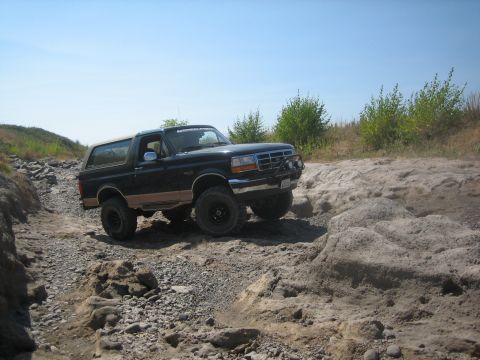 1995 Ford Bronco - A 1995 Ford Bronco navigates a rocky off-road trail under a clear blue sky.
