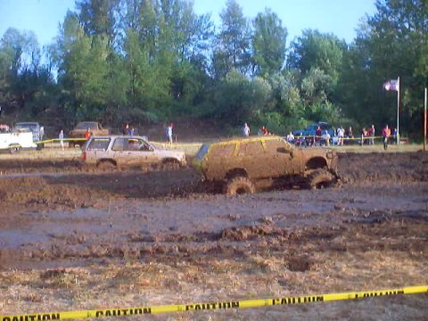 1976 Ford F-100 - Multiple vehicles navigate a muddy track during an off-road competition.