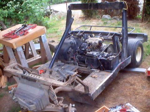1976 Ford F-100 - A homebuilt buggy under construction in a grassy backyard: a stripped black tube frame with roll bar and rear cage carries a small horizont…