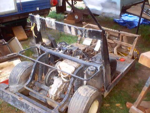 1976 Ford F-100 - Rear three-quarter view of a stripped homebuilt go-kart or buggy chassis sitting on grass, showing a tube roll cage, a small engine and tra…