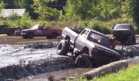 1979 Ford Bronco - Several trucks and an ATV navigate a muddy obstacle course during a daytime event.