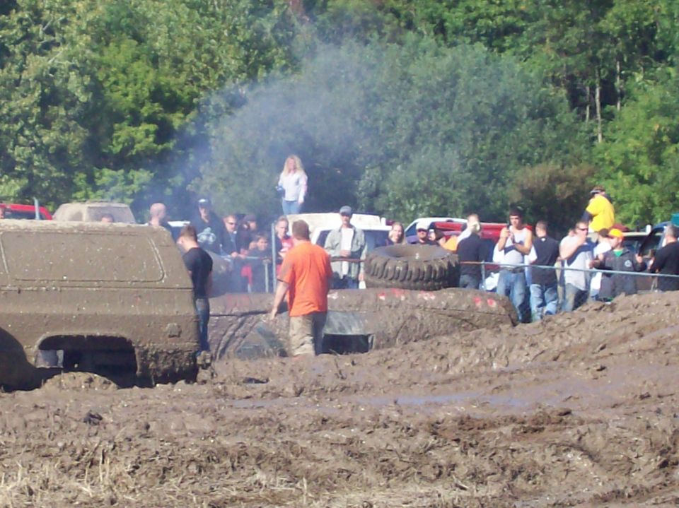 Mud bogging event with several off-road vehicles stuck in deep mud, spectators watching