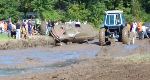 1979 Ford Bronco - A blue tractor assists a stuck vehicle in a muddy off-road event.