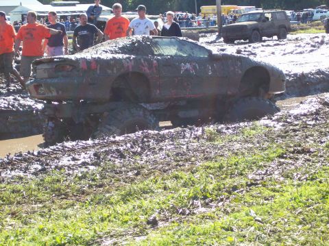 1979 Ford Bronco - A heavily mud-caked car is stuck in a muddy terrain, with spectators in the background.