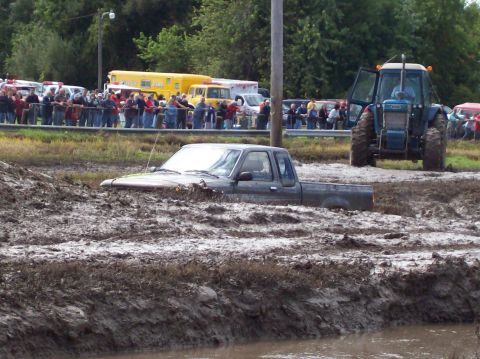 1979 Ford Bronco - A pickup truck is stuck in deep mud, with a tractor and spectators in the background.