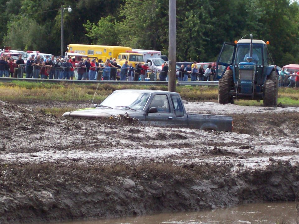 Gray pickup truck submerged in mud with a blue tractor nearby