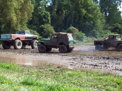 1979 Ford Bronco - Modified trucks and SUVs navigate a challenging muddy terrain during an off-road event.