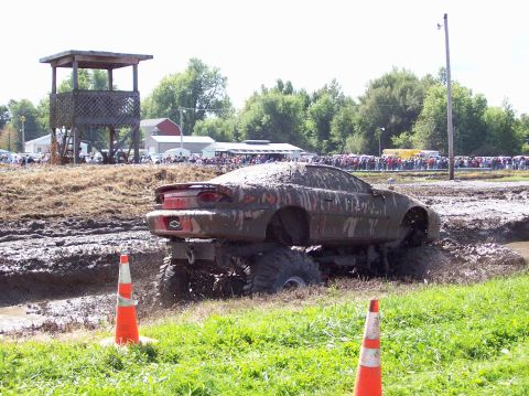 1979 Ford Bronco - A car modified with a monster truck chassis navigates a mud pit during an event.