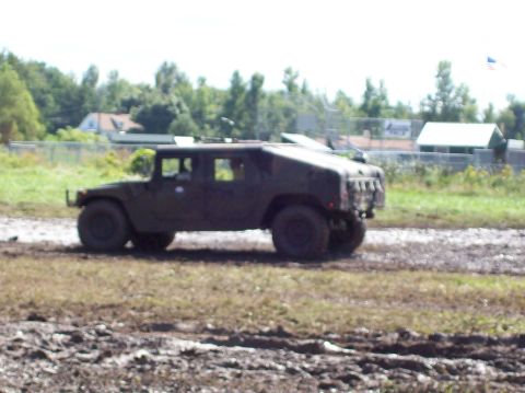 1979 Ford Bronco - Humvee navigates a muddy terrain under a partly cloudy sky.
