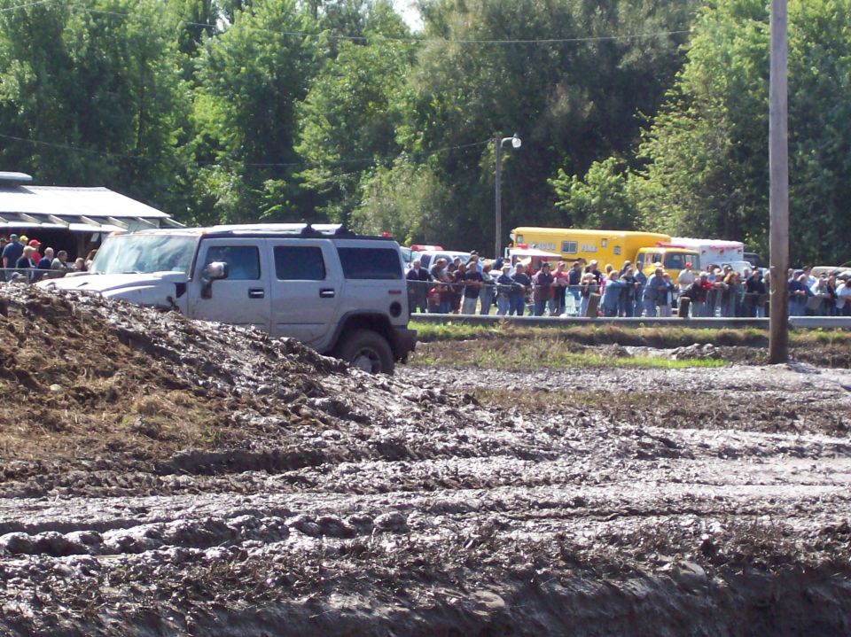 Silver Hummer H2 stuck in a mud pit with a crowd watching