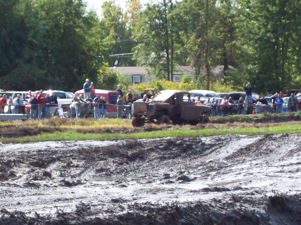 Mud bogging event with spectators and vehicles in the background