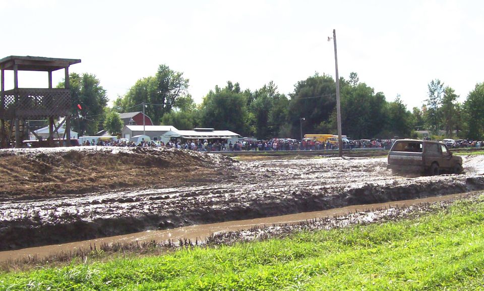 1979 Ford Bronco driving through mud at an event with spectators and a wooden tower