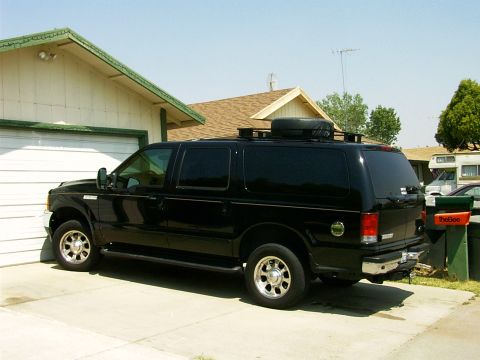 2000 Ford Excursion - A black 2000 Ford Excursion is parked in front of a garage, showing its side profile and roof rack.