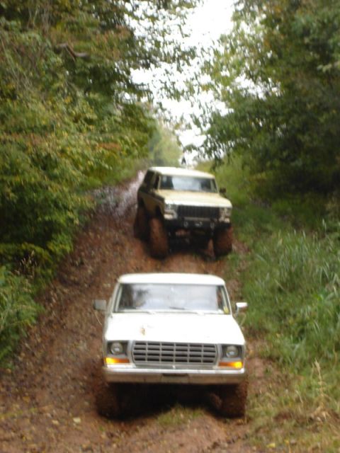 1992 Ford Mustang - Two off-road vehicles, a white Ford F-Series truck and a tan SUV, navigate a muddy trail through a wooded area.