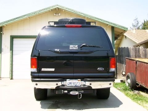 2000 Ford Excursion - Rear view of a black 2000 Ford Excursion, a roof rack and a trailer hitch, parked in front of a garage.
