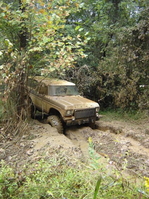 1992 Ford Mustang - A brown 1978 Ford Bronco navigates a muddy trail, its tires deep in the mire.