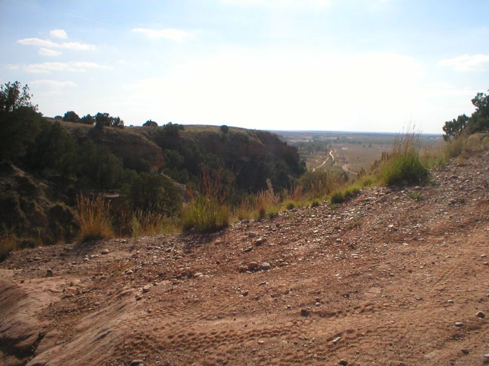 Dirt road winding through a canyon landscape under a bright sky