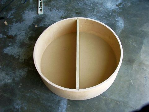 2000 Ford Excursion - A custom-built circular speaker box with a central divider, likely made of MDF or plywood, sits on a concrete floor.