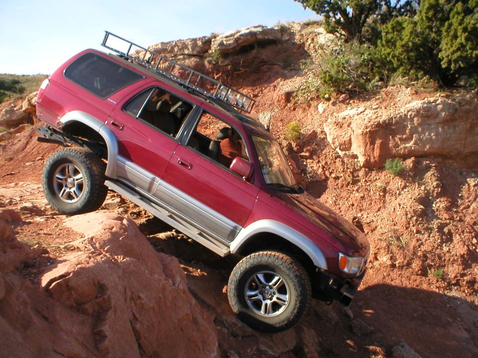 1996 Toyota 4Runner climbing a steep, rocky hill. The vehicle has a roof rack and aftermarket wheels
