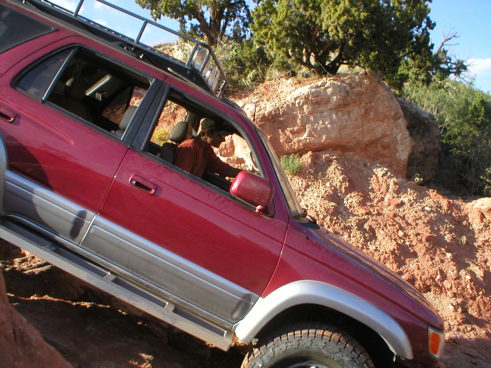Red SUV climbing rocky terrain, driver visible inside