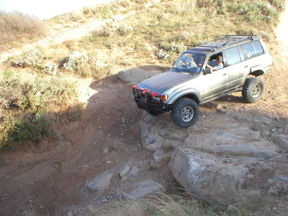 Silver Toyota Land Cruiser off-roading on rocks, front bumper modified with a winch guard
