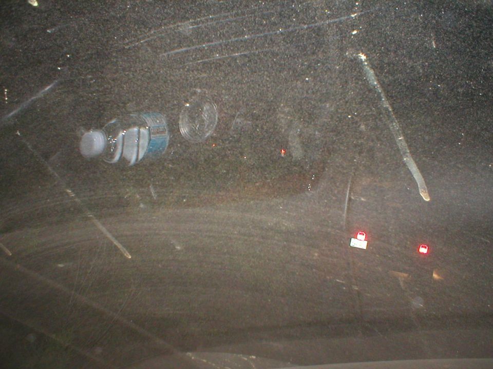 Water bottle and cup on a dirty dashboard, seen through the windshield at night