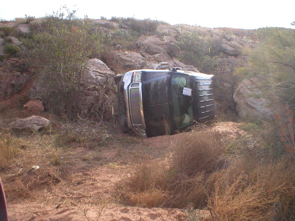 Overturned dark 1996 Toyota 4Runner on its side in a rocky, dry landscape