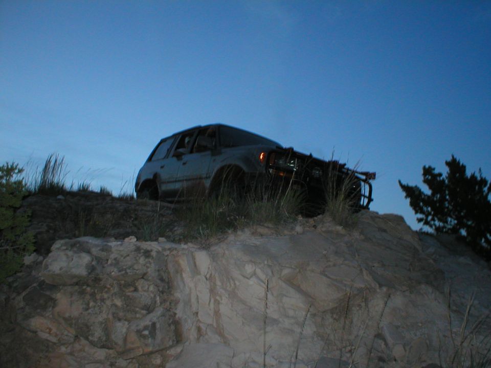Gray SUV with a brush guard on a rocky incline under a clear blue sky