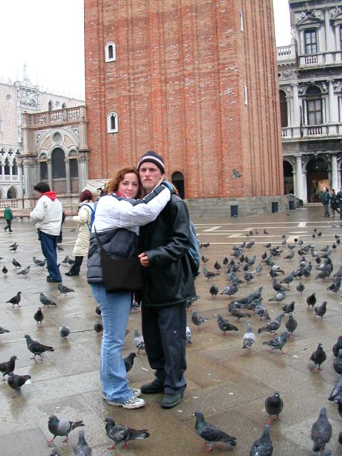 1984 Ford Bronco - A couple hugs in St. Mark's Square, Venice, with pigeons flocking around them and historic buildings in the background.